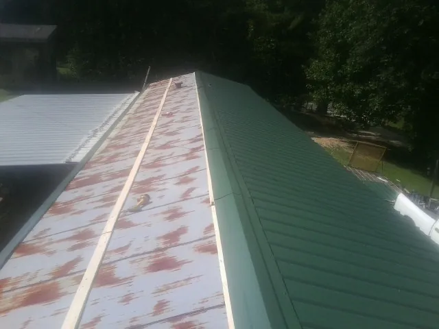 Old rusted panels beside newly installed green metal roofing — Wind Damage Roof Repair by Roofing Brothers in Clifton
